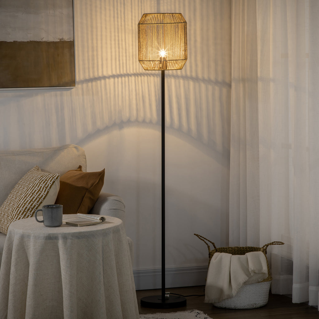 Lámpara de pie con pantalla de cuerda de papel encendida junto a una mesa con mantel y una cesta
