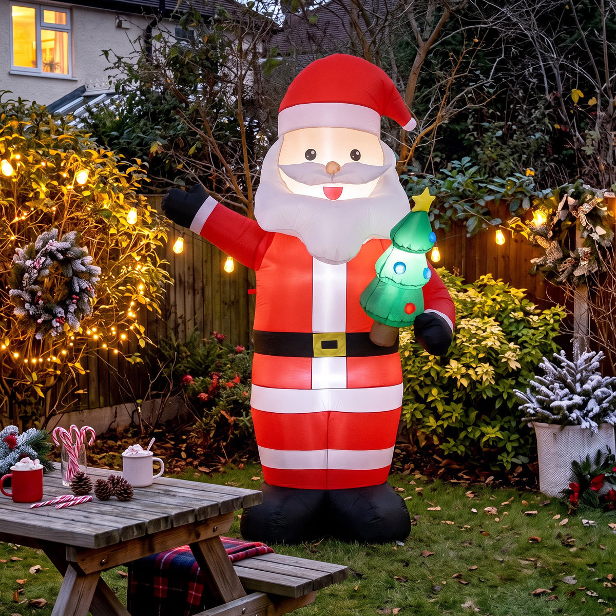 Papá Noel hinchable de 243 cm en un jardín decorado con luces y una mesa de madera