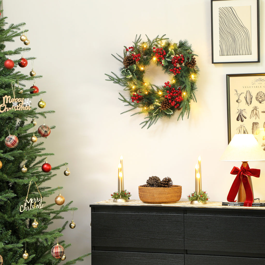 Corona de Navidad con luces cálidas colgada en una pared blanca junto a un árbol de Navidad y una cómoda negra