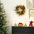 Corona de Navidad con luces cálidas colgada en una pared blanca junto a un árbol de Navidad y una cómoda negra