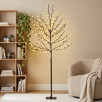 Árbol de cerezo luminoso con luz blanca cálida junto a una estantería de madera y un sillón