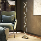 Lámpara de pie LED de doble espiral encendida junto a un sillón verde en un salón