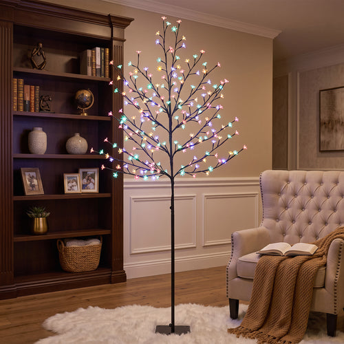 Árbol de cerezo luminoso multicolor junto a una estantería y un sillón en un salón