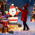 Niña mirando el Papá Noel luminoso en un jardín nevado con regalos