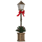 Farol de Navidad LED con linterna de bronce, lazo rojo y pequeño árbol verde en una maceta, vista frontal sobre fondo blanco