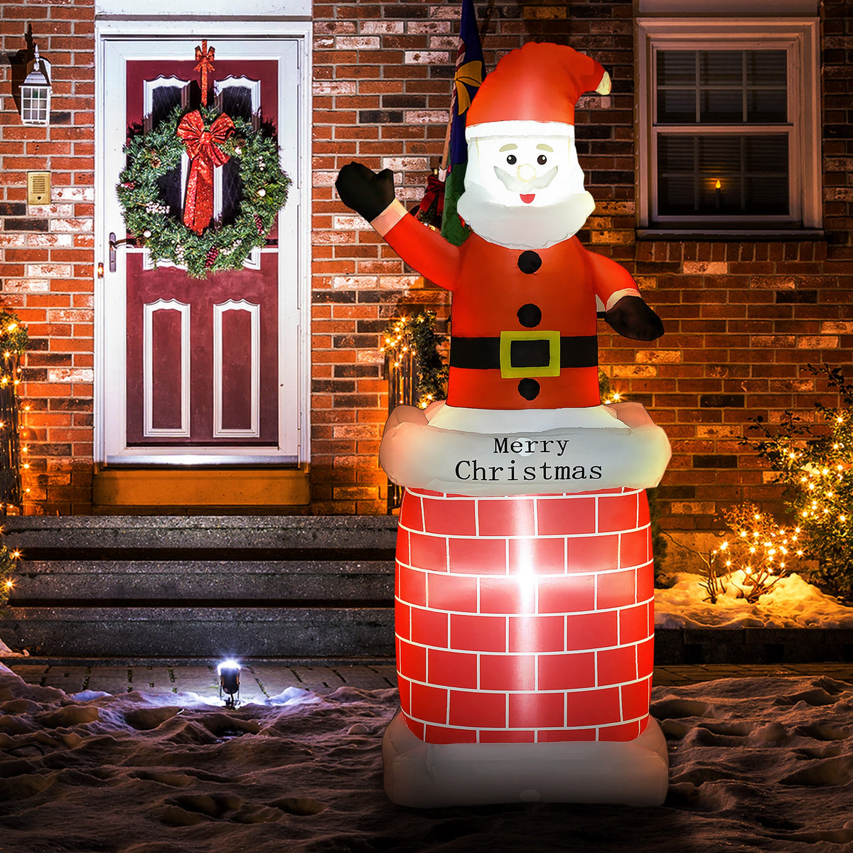 Papá Noel hinchable en una chimenea junto a una puerta con corona navideña por la noche