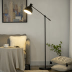 Lámpara de pie negra encendida junto a un sillón gris con cojines y una planta