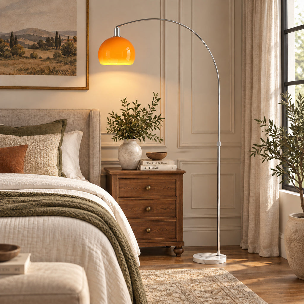 Lámpara de pie en arco naranja junto a una cama con mesilla de madera, planta y ropa de cama beige