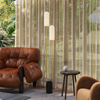 Lámpara de pie dorada con pantallas de vidrio encendidas junto a un sillón de cuero y una mesa redonda