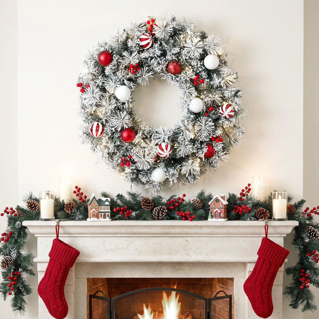 Corona de Navidad nevada sobre una chimenea decorada con guirnalda y calcetines rojos