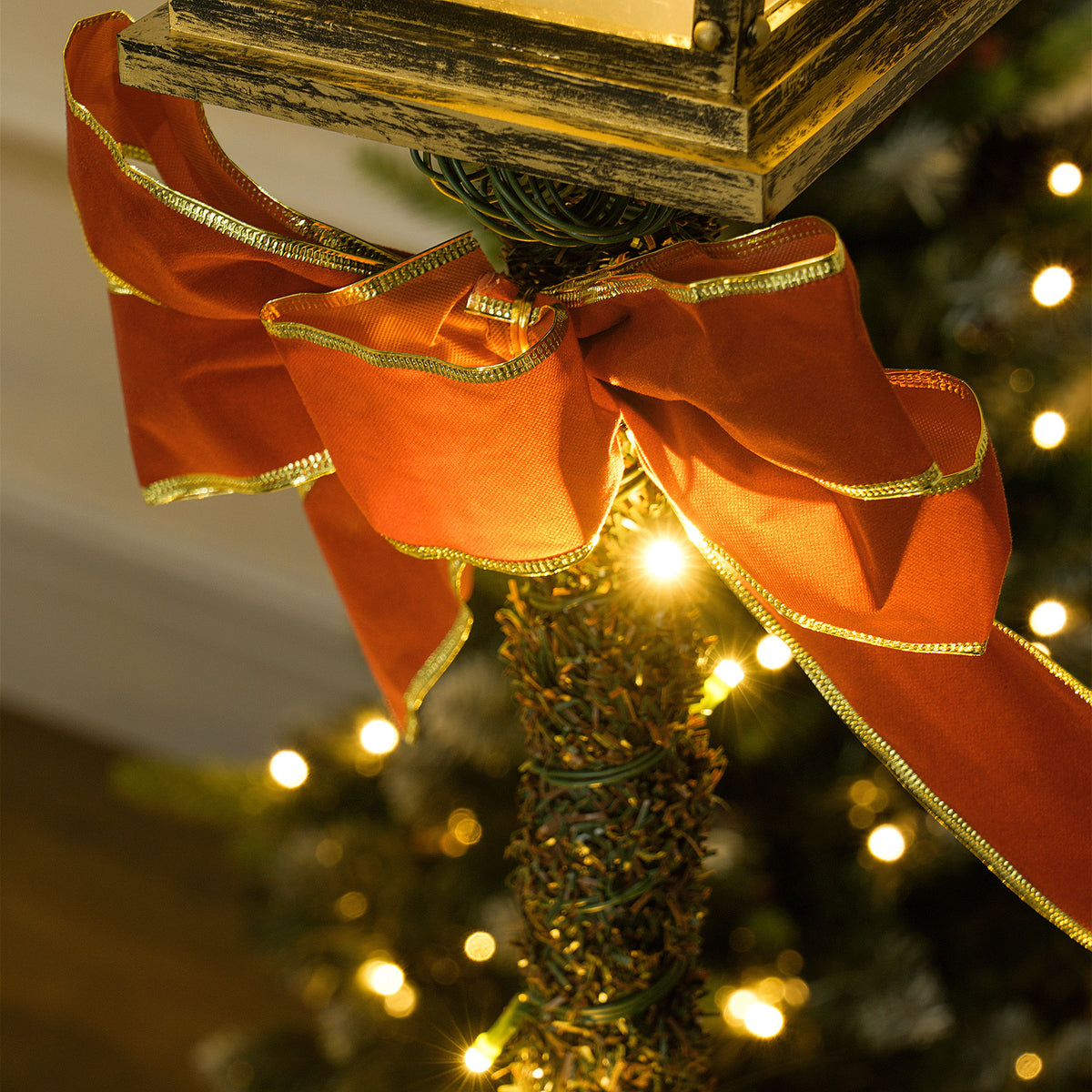 Detalle del lazo rojo con borde dorado del farol de Navidad LED y las luces del árbol