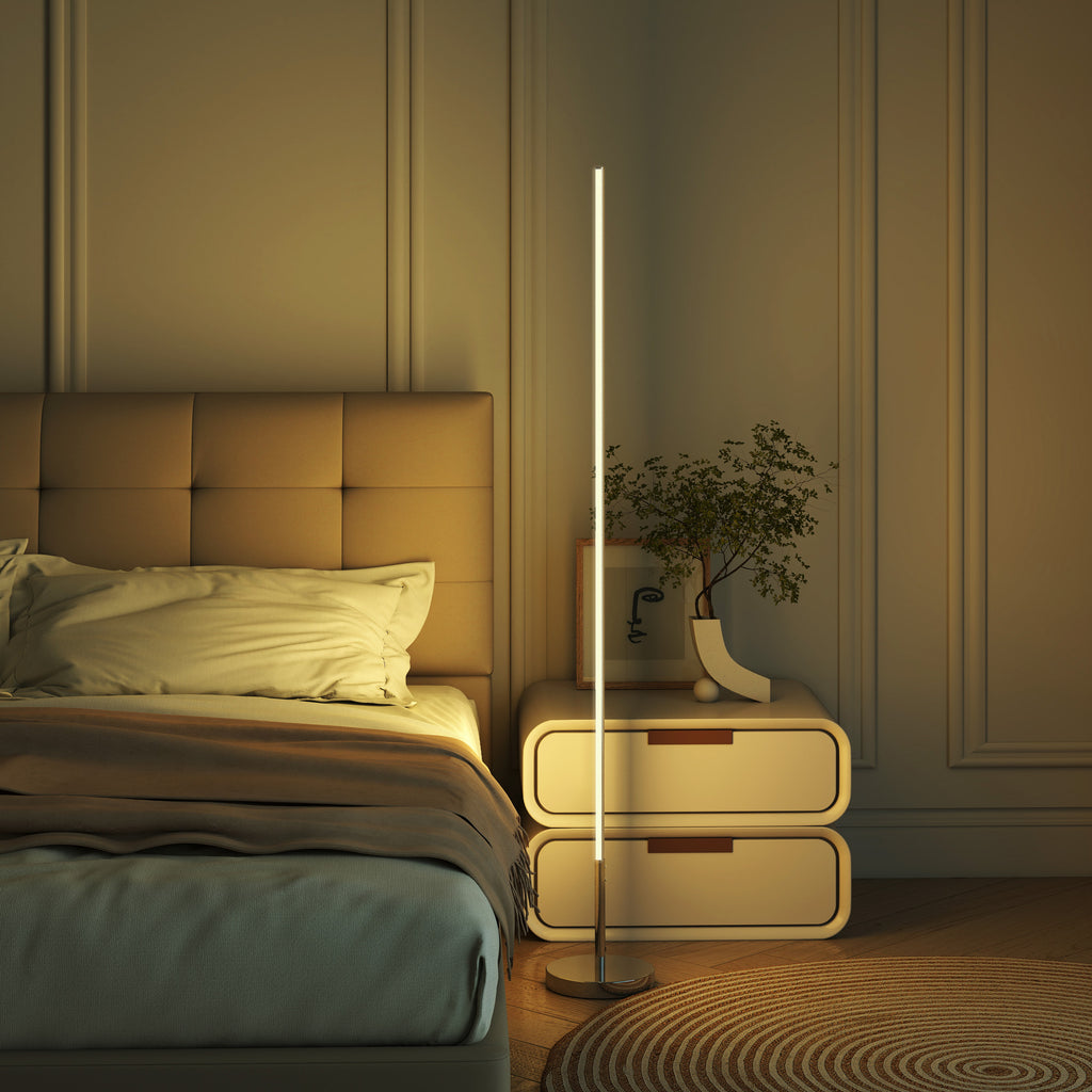 Lámpara de pie LED encendida junto a una cama y una mesita en un dormitorio