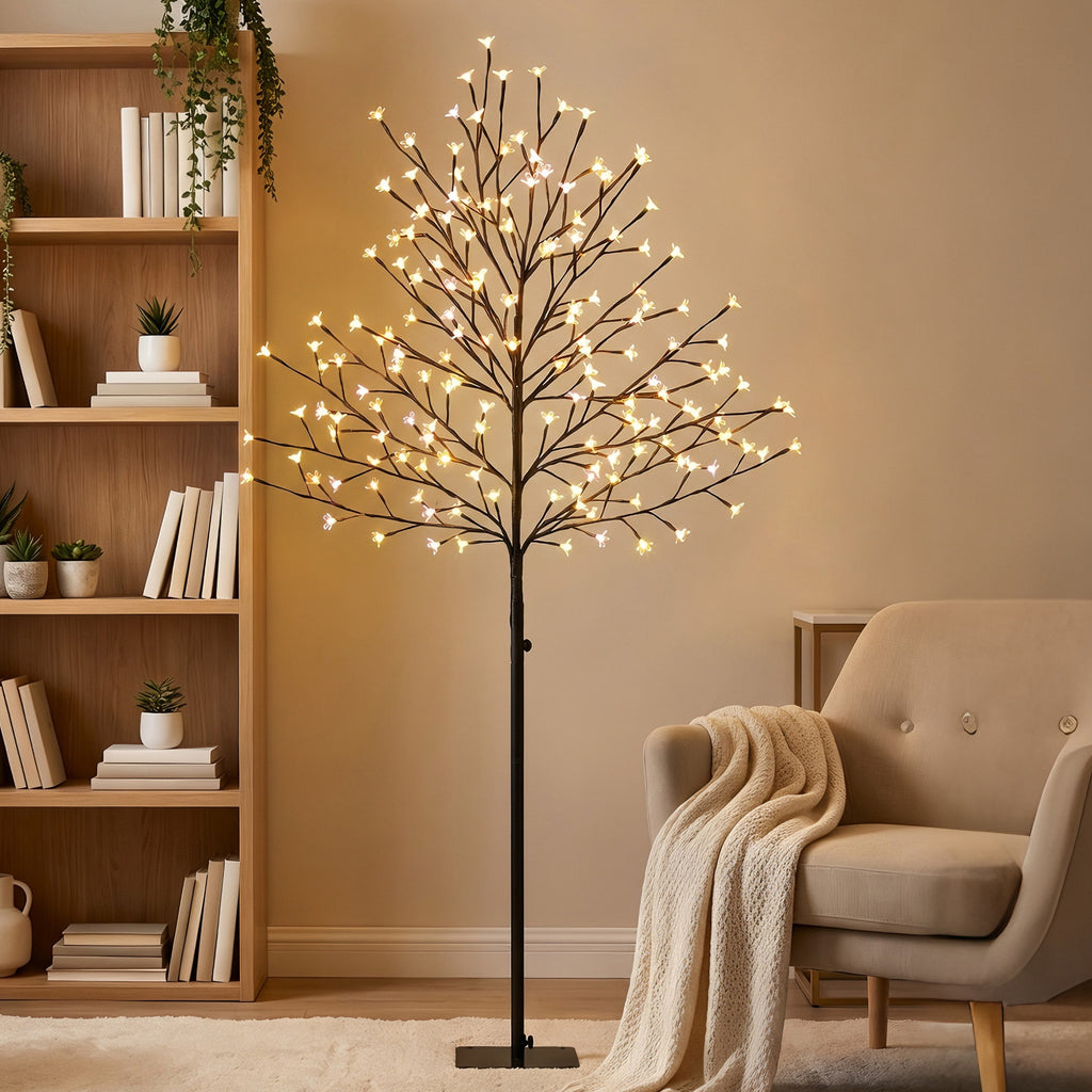 Árbol de cerezo luminoso con luz cálida junto a una estantería y una manta en el salón