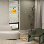 Lámpara de pie en arco con pantalla naranja sobre un sofá redondo crema y un sillón verde