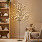 Árbol de cerezo luminoso encendido con luz cálida junto a una estantería y un sillón en un salón