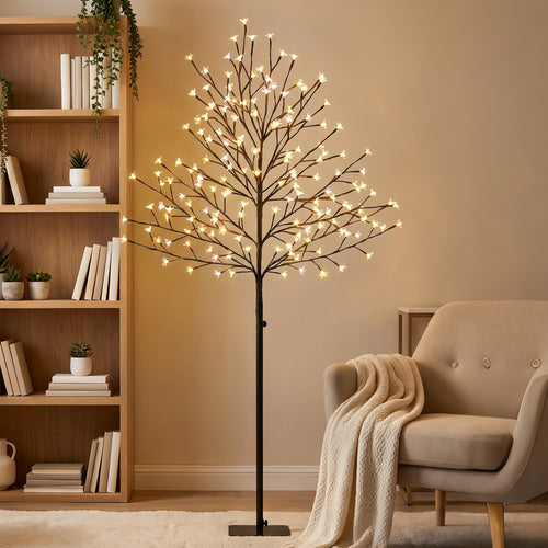 Árbol de cerezo luminoso encendido con luz cálida junto a una estantería y un sillón en un salón