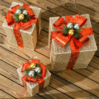 Tres cajas de regalo doradas con lazo rojo y bolas plateadas y doradas sobre una terraza de madera