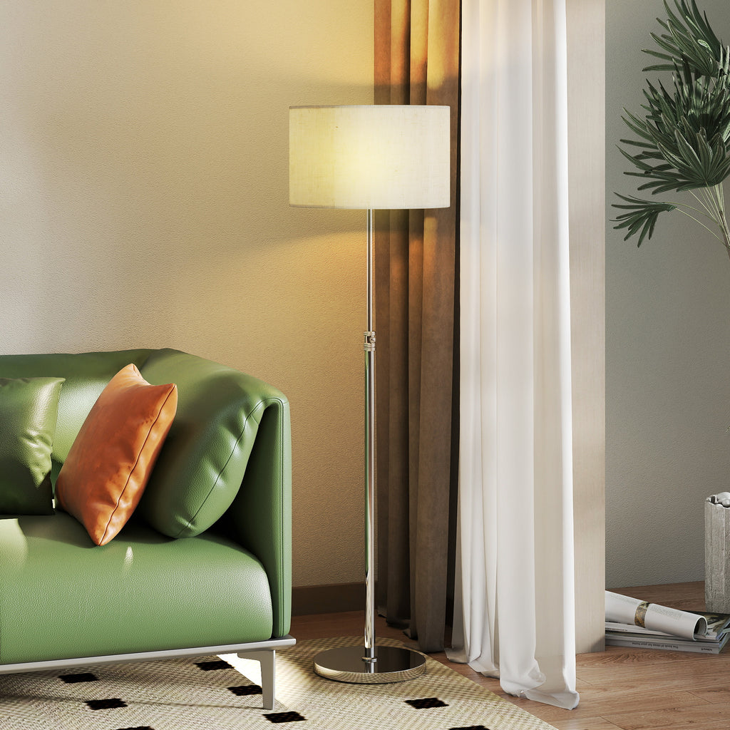 Lámpara de pie plateada encendida con luz cálida junto a un sillón verde y una cortina