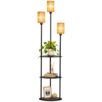 Lámpara de pie boho negra con tres luces encendidas y una planta en el estante, sobre fondo blanco